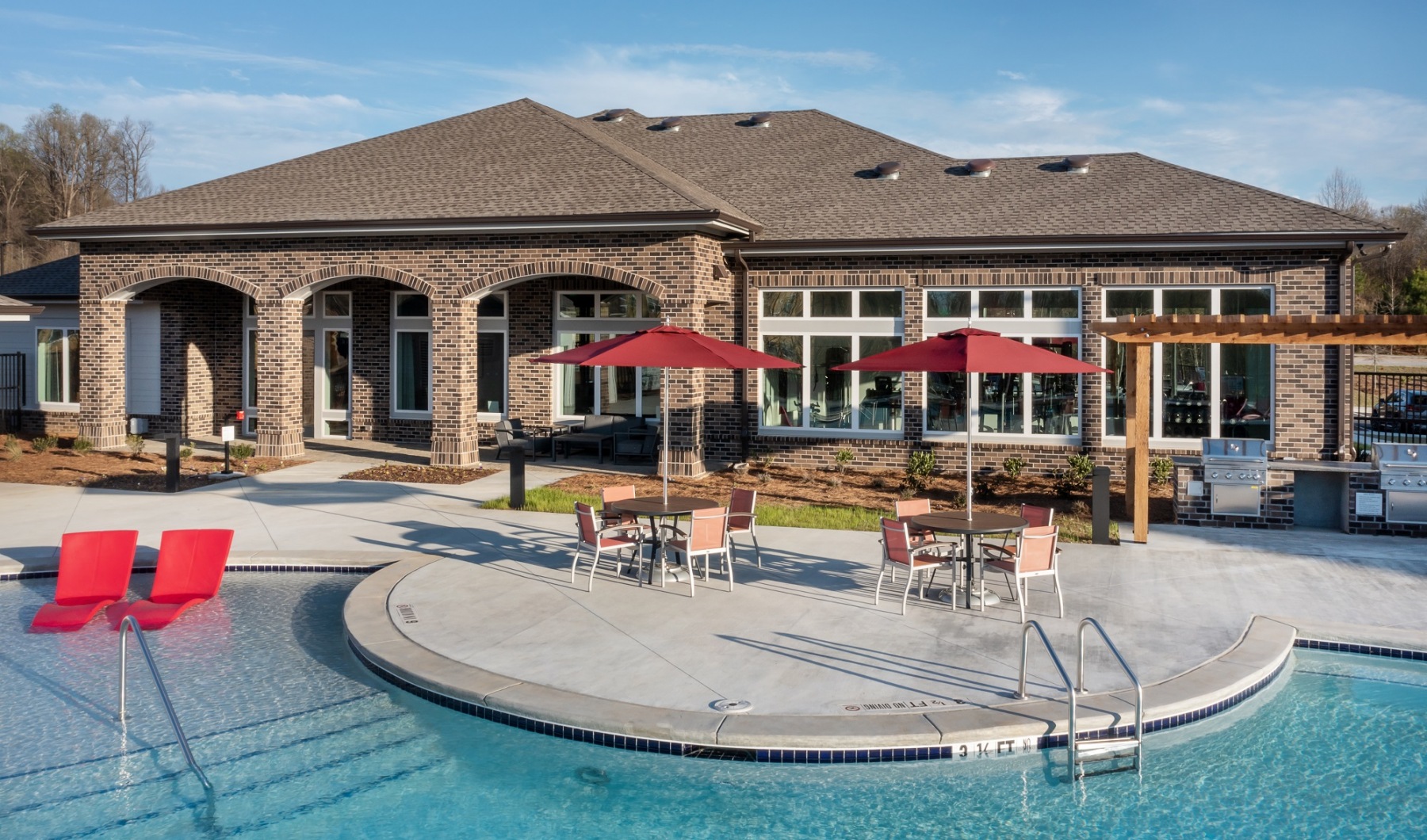The pool area at our apartments in Jefferson, featuring outdoor tables with chairs and umbrellas, and a clubhouse. 